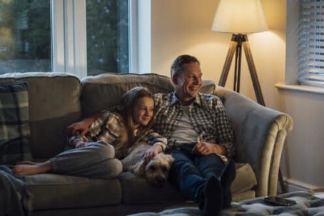 A couple relaxes on a sofa with their dog
