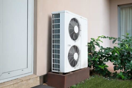 Outdoor dual-fan HVAC unit next to a wall